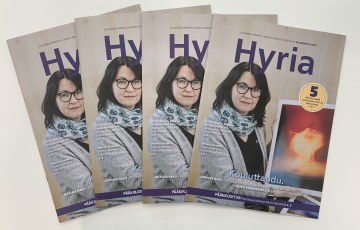 4 Hyria-lehteä viuhkamuodostelmassa pöydällä. Kannes nainen esittelee taidevalokuvaa