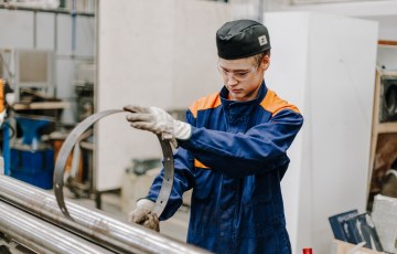 Työhaalariin pukeutunut levyseppähitsaajaopiskelija mankeloi metallista rengasta.