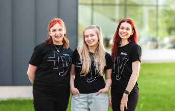 Valokuva, jossa on kolme naista. Naiset seisovat vierekkäin. Naiset katsovat kameraan ja hymyilevät. Heillä on päällään t-paidat, joissa on Hyrian logo.