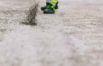 Henkilö hiekoittaa kiinteistön pihaa lapio ja ämpäri käsissään