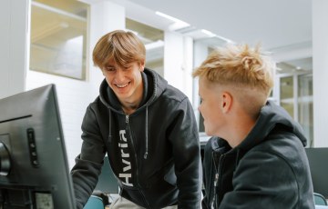 kaksi nuorta Hyrian huppareissa tietokoneen ääressä