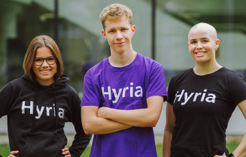 Kolme nuorta seisoo rivissä, hymyilee ja katsoo kameraan.
