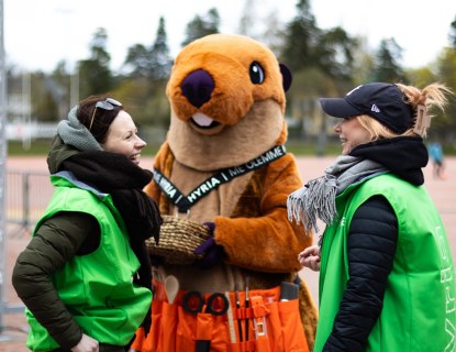 Hyrian kaksi henkilökunnan jäsenta yhdessä maskotti Heimo majavan kanssa ulkona.