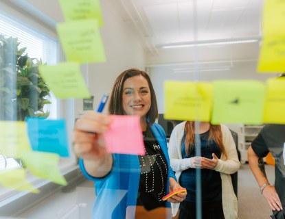 Anna Skytten laittaa toimistotilassa post-it lappua lasiseinään kiinni. 