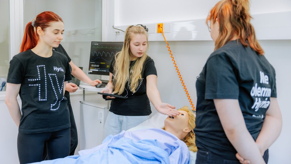 Lähihoitajaopiskelijat hoitoluokassa hoitamassa hoitonukkea.