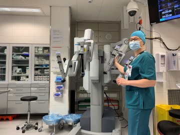 Sairaanhoitaja leikkaussalissa leikkausrobotin vieressä työasussaan maski kasvoilla.