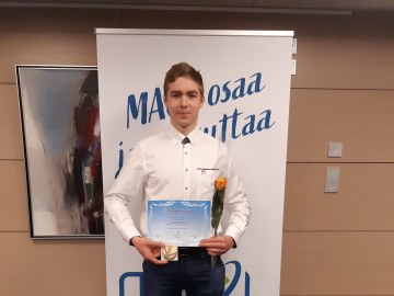 Nuori mies pitelee mitalia ja kunniakirjaa sekä ruusua rollupin edessä.