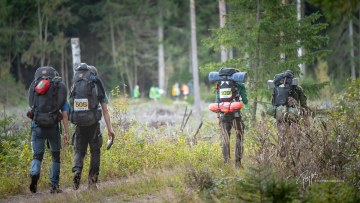 Retkeilijöitä menossa maastoon metsässä rinkat selässä.